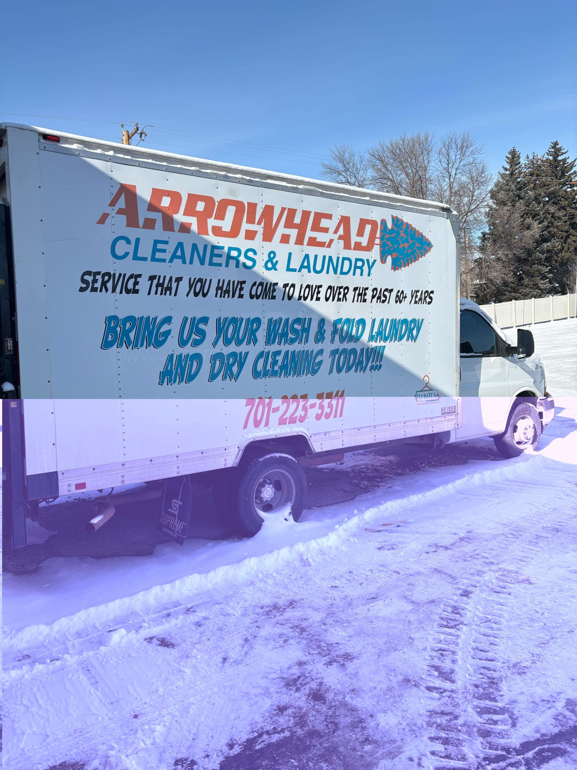 Box truck for Arrowhead Cleaners & Laundry on a snowy street, displaying text about laundry and dry cleaning services and a phone number.