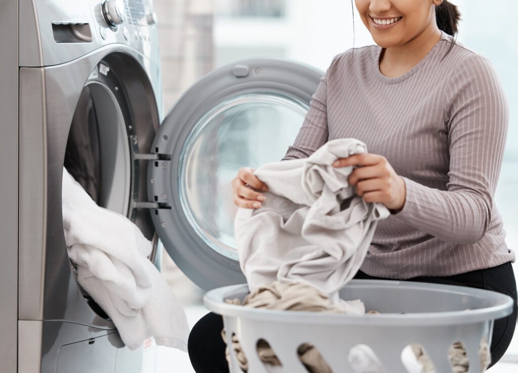 A person smiling while unloading a front-loading washing machine into a laundry basket.