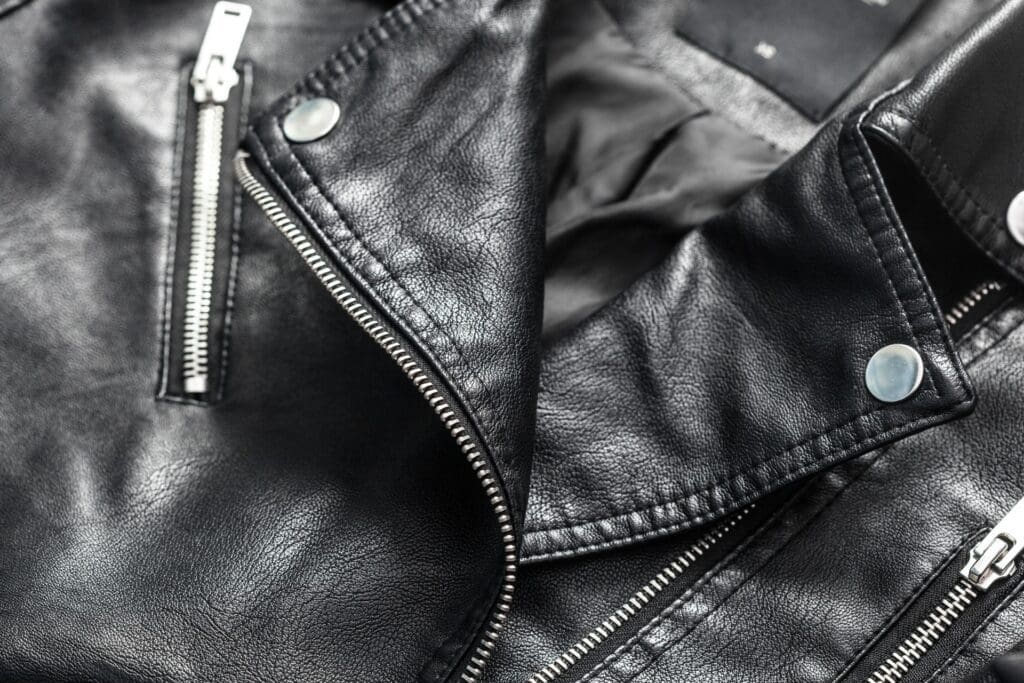 Close-up of a black leather jacket showing silver zippers, snap buttons, and textured leather material.