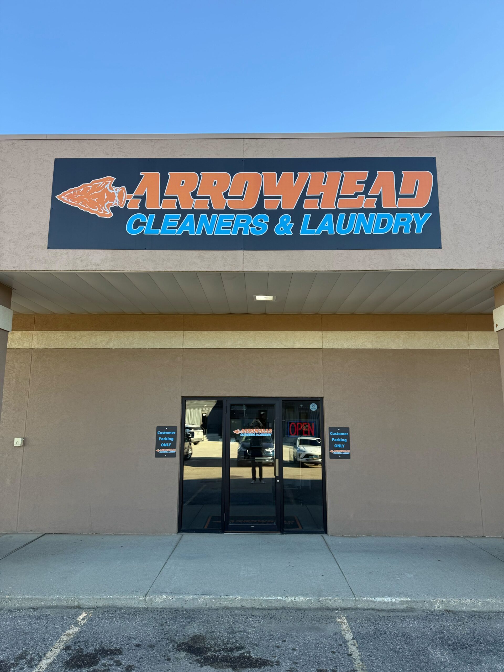 The storefront of Arrowhead Cleaners & Laundry with a large sign above the entrance and glass double doors below.