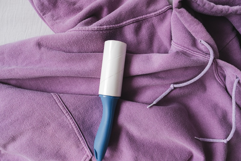 A lint roller with a blue handle rests on a purple hoodie.