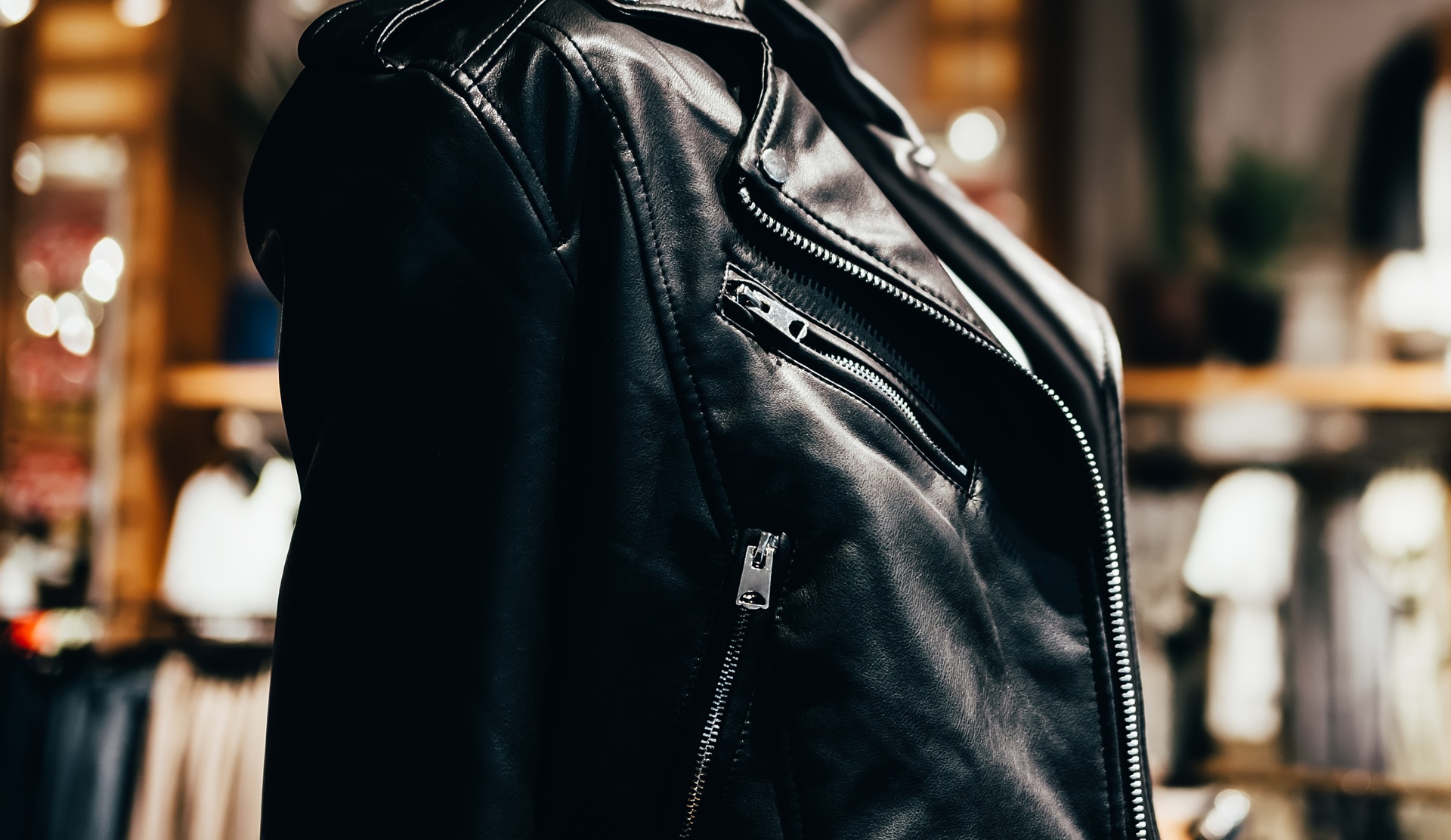 Close-up of a black leather jacket with visible zippers on a blurred indoor background.