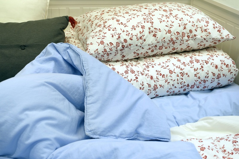 A neatly made bed with two floral-patterned pillows and a light blue comforter, against a white paneled wall.